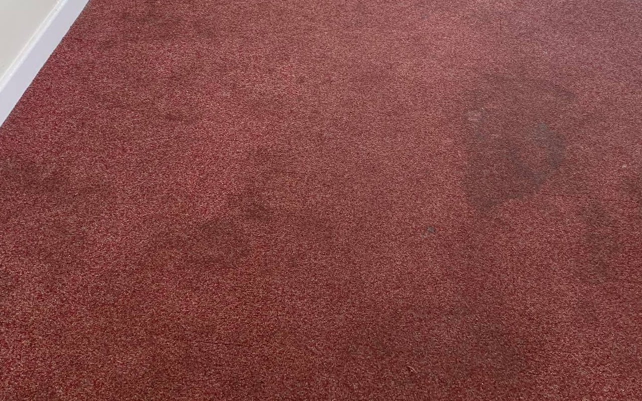 A coffee stain on a red carpet before cleaning by Jay's Cleaning